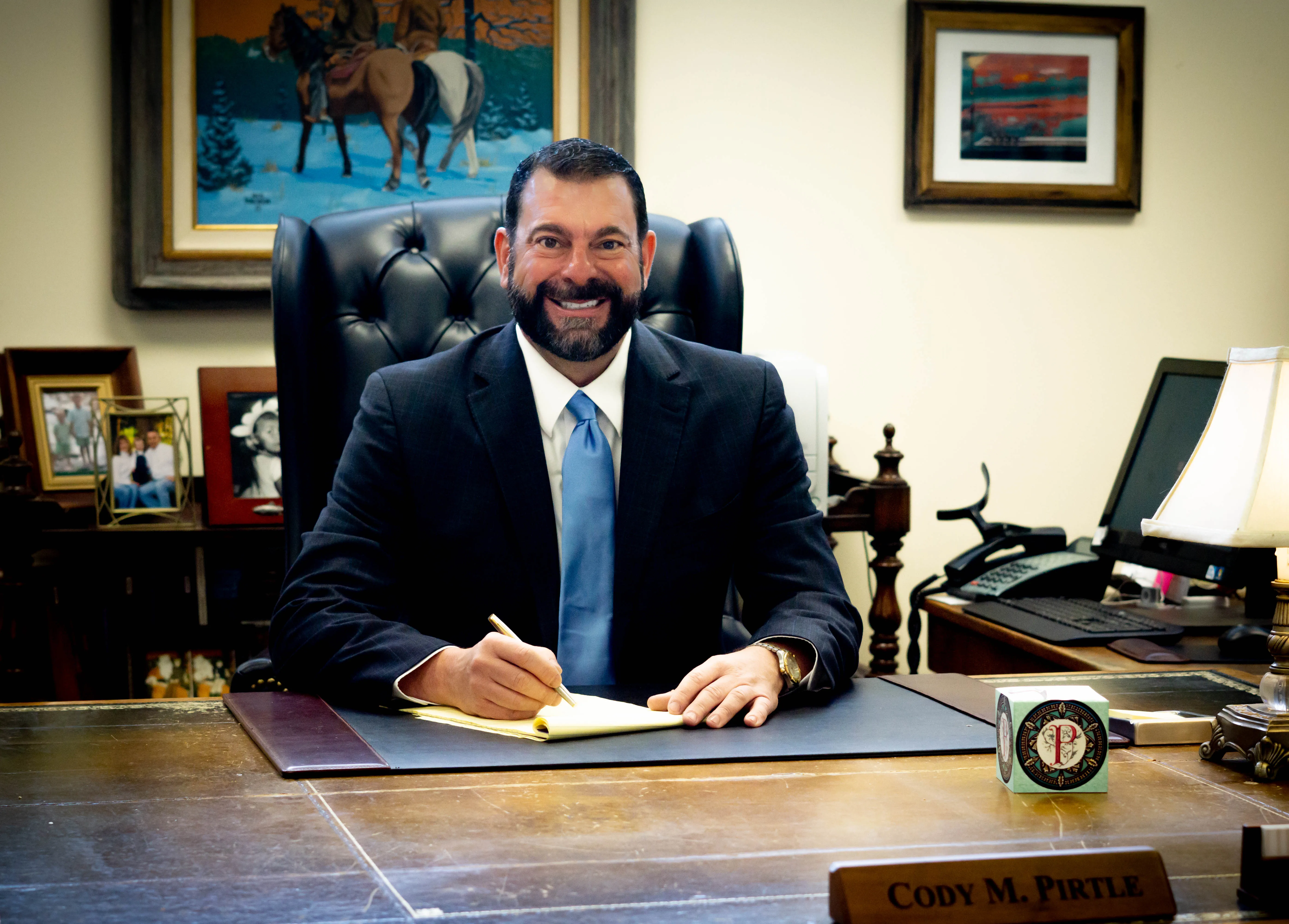 Cody Pirtle sitting at desk with paper and pencil in hand, smiling towards you.